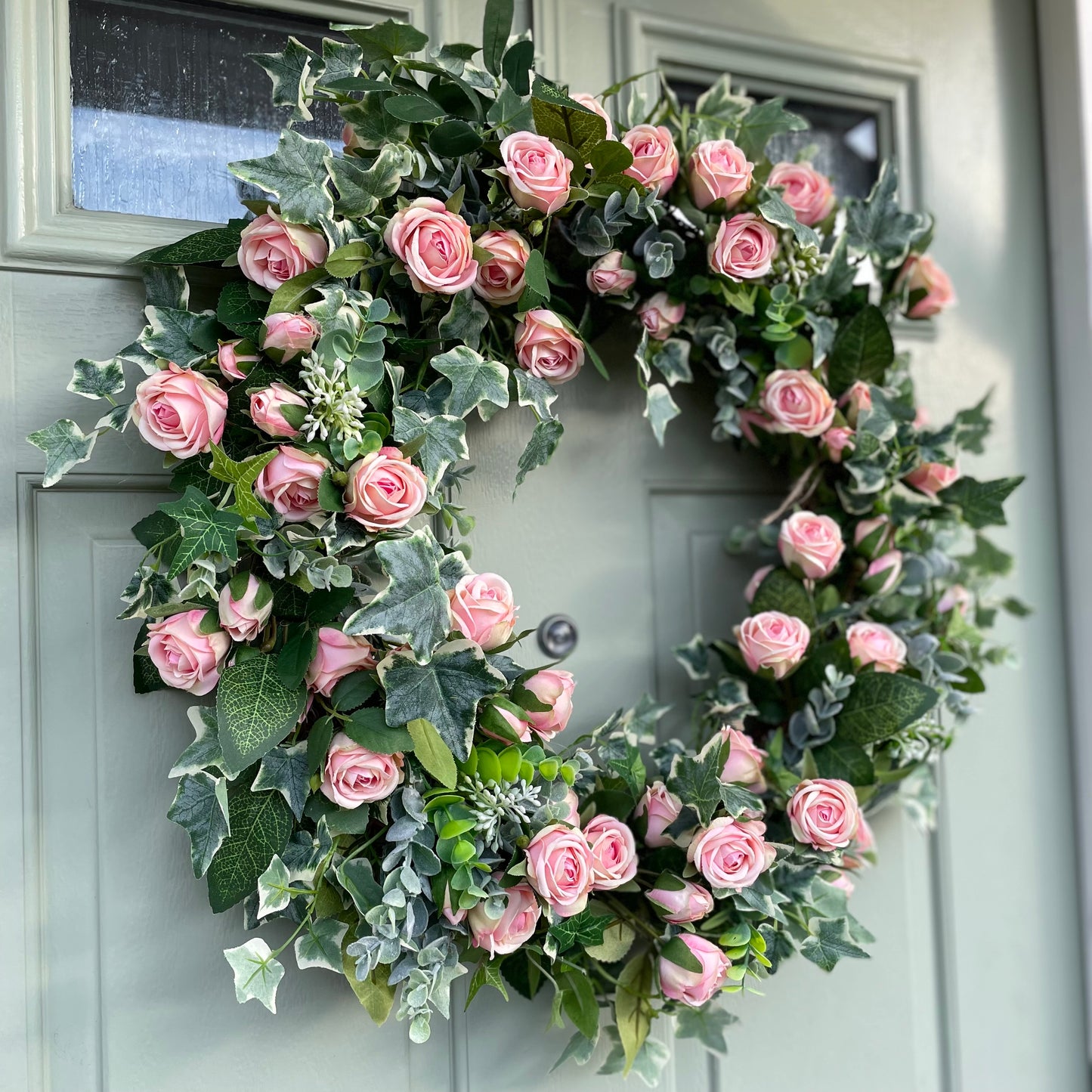 Summer faux wreath with pink roses. ivy and eucalyptus foliage styled on a rustic cottage door.
