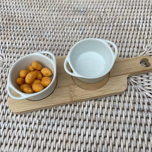 Wooden serving board with two white ceramic dipping dishes, styled for entertaining at home.