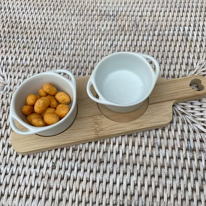 Wooden serving board with two white ceramic dipping dishes, styled for entertaining at home.