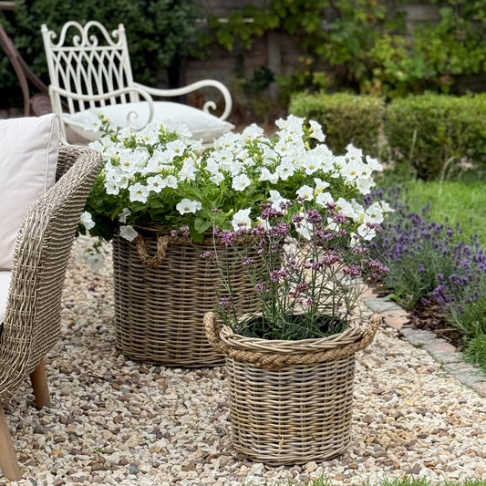 Two rattan planters with flowers on a pebble garden path