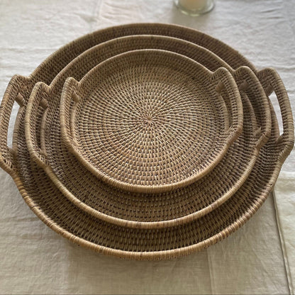 Set of three woven round rattan trays on a linen table cloth.