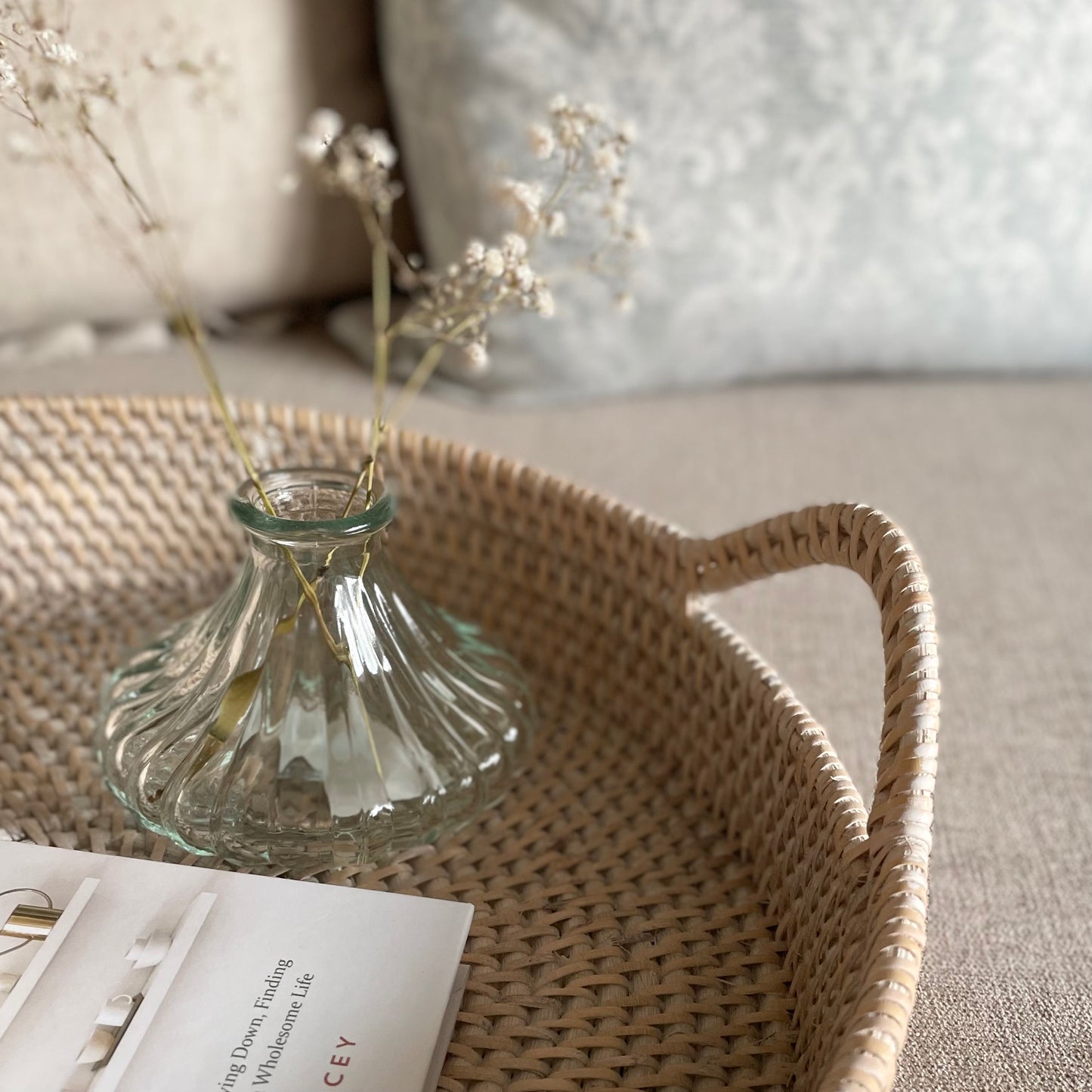 Whitewashed round rattan tray with handles styled on a neutral sofa with home accessories.