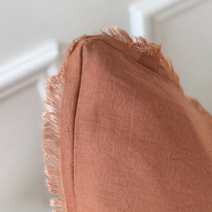 Close-up of a rust coloured cushion with frayed edges on a white background.
