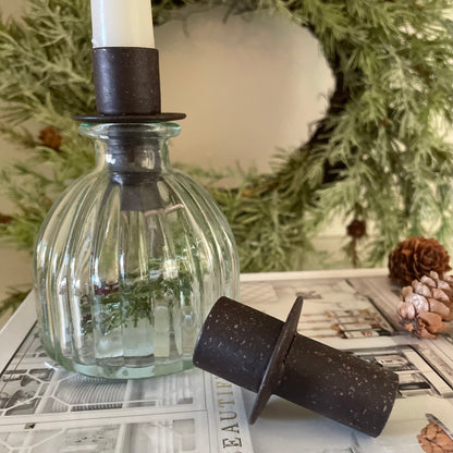 Rustic metal bottle top candle holder placed in a glass bud vase. Styled on a book.