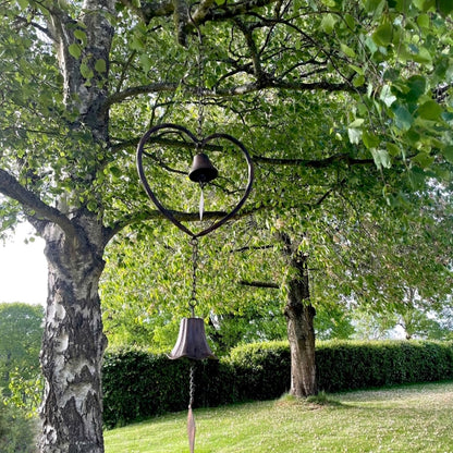 Handmade vintage style heart wind chime with delicate bells, hanging outdoors in a rustic garden setting.