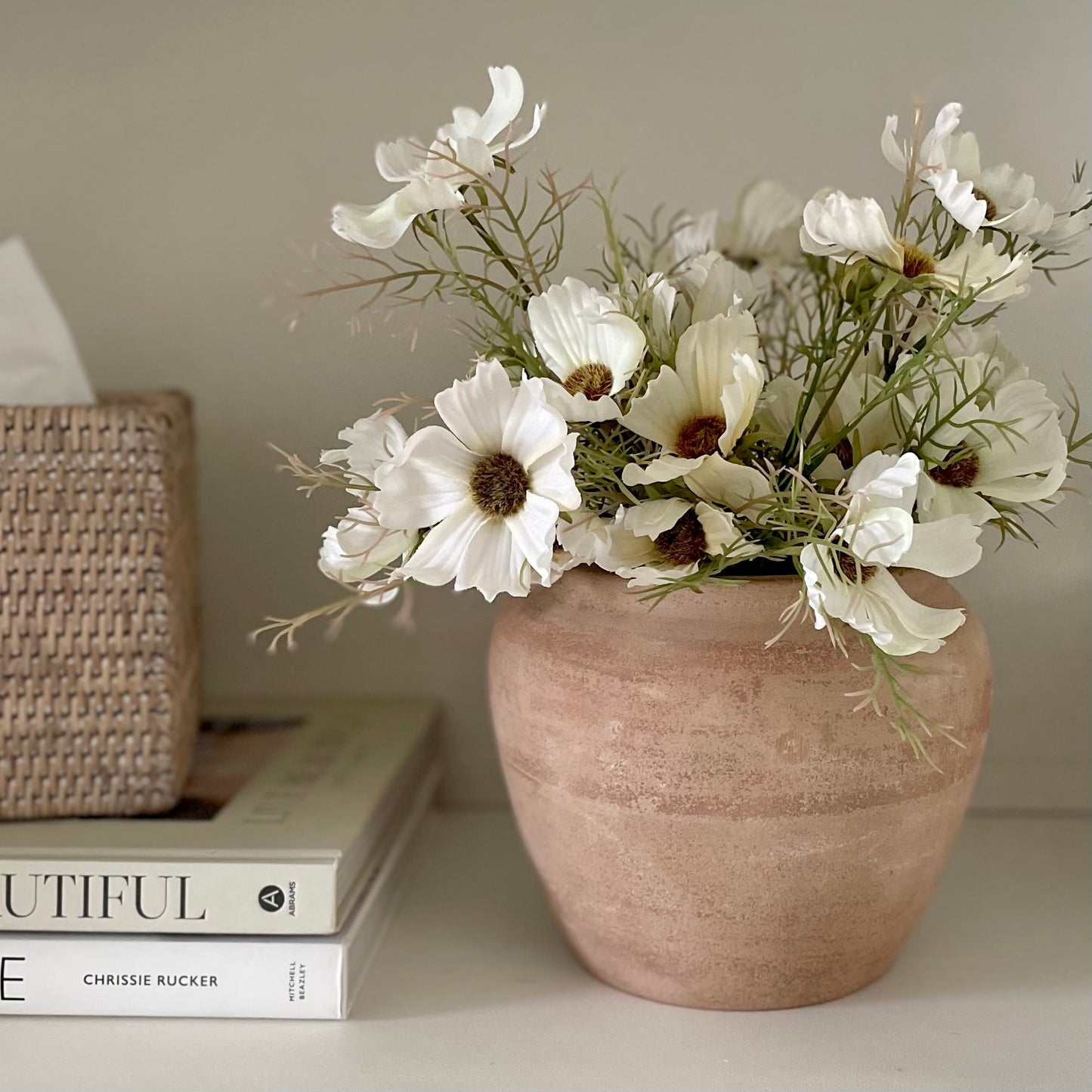 Rustic unglazed terracotta Henley pot with natural finish. Styled with cosmos spray on a shelf with books and rattan tissue box.