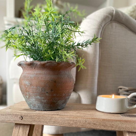 Rustic terracotta plant pot with pie crust edge. Styled on wooden stool and candle, in a cosy living rom.