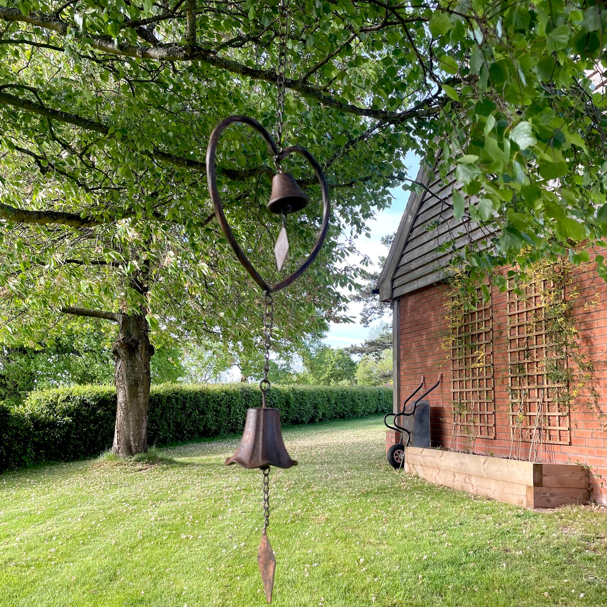 Handmade vintage style heart wind chime with delicate bells, hanging outdoors in a rustic garden setting.