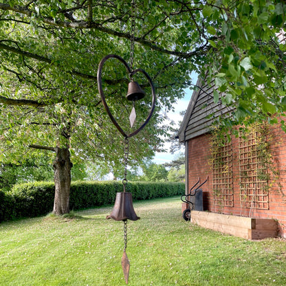Handmade vintage style heart wind chime with delicate bells, hanging outdoors in a rustic garden setting.