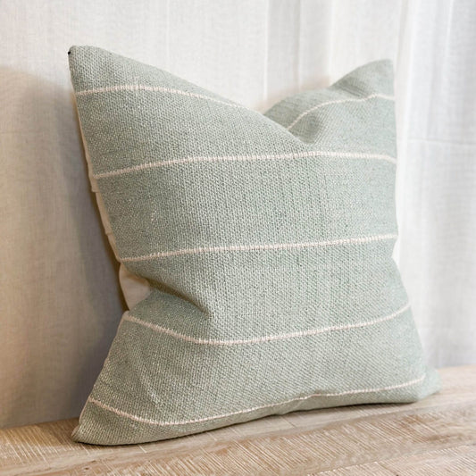 Sage green and cream striped cotton cushion styled on a neutral sofa with a throw.