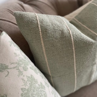 Sage green and cream striped cotton textured cushion, styled on a neutral sofa with a throw.
