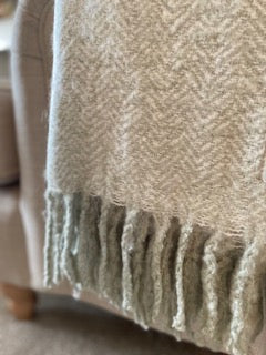 Soft sage green herringbone mohair feel throw with fringed edges draped over a sofa.