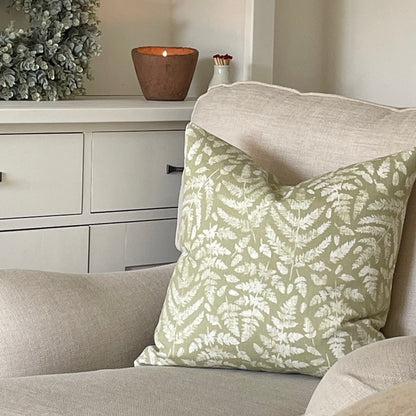 Sage green cushion with fern leaf detailing styled on a neutral armchair with a throw.