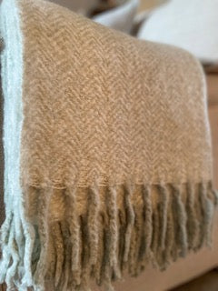 Soft sage green herringbone mohair feel throw with fringed edges draped over a sofa, adding warmth and texture to a cosy living room.
