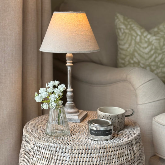Small table with lamp, mug, scented candle and flowers in a cosy room.