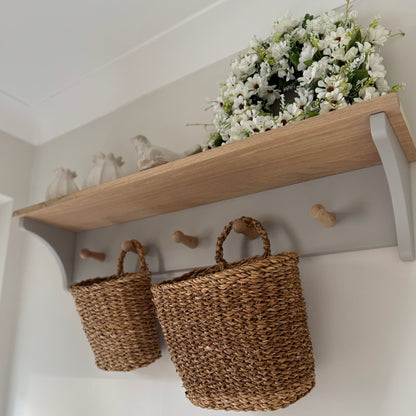 Wooden shelf with wicker baskets and a floral arrangement on a white wall.