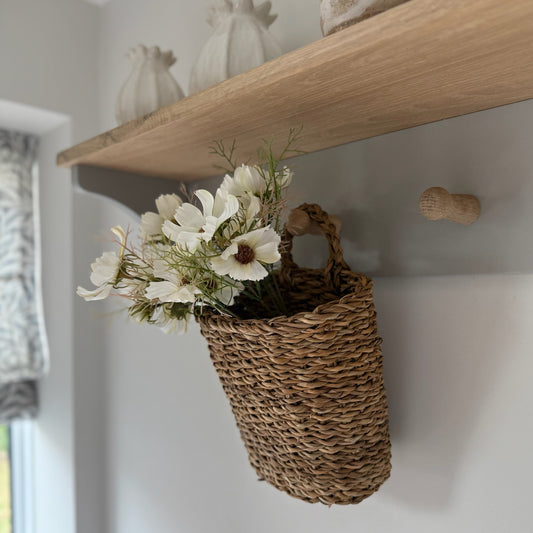 Handwoven seagrass hanging baskets with handles, styled on a peg rail and filled with dried flowers for a rustic, natural look.