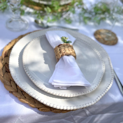 Woven hyacinth napkin ring holding a neutral linen napkin, showing its natural texture and rustic, organic finish. Styled on a garden dining table.