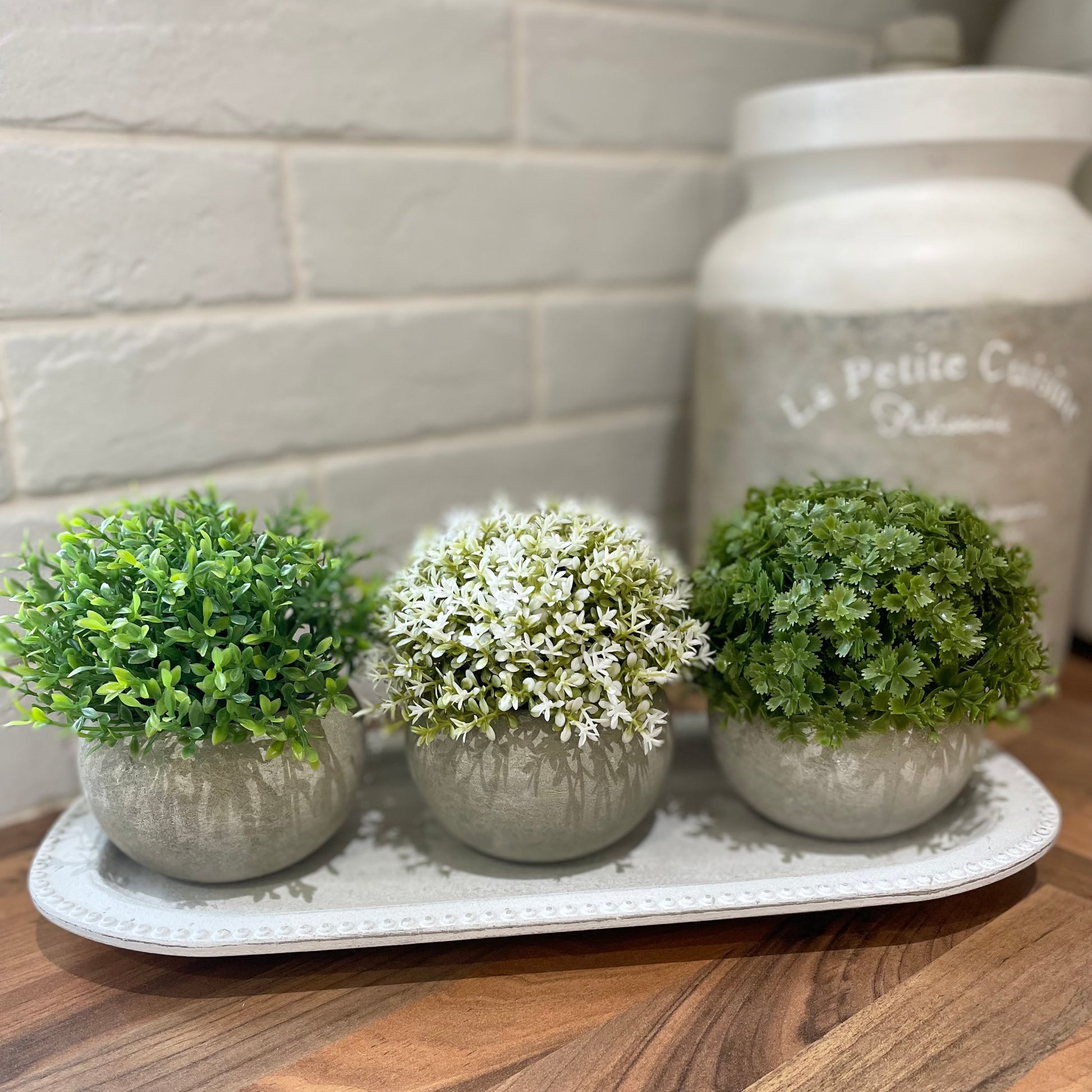 Faux green Hebe bush in a cement pot styled on a wooden tray.