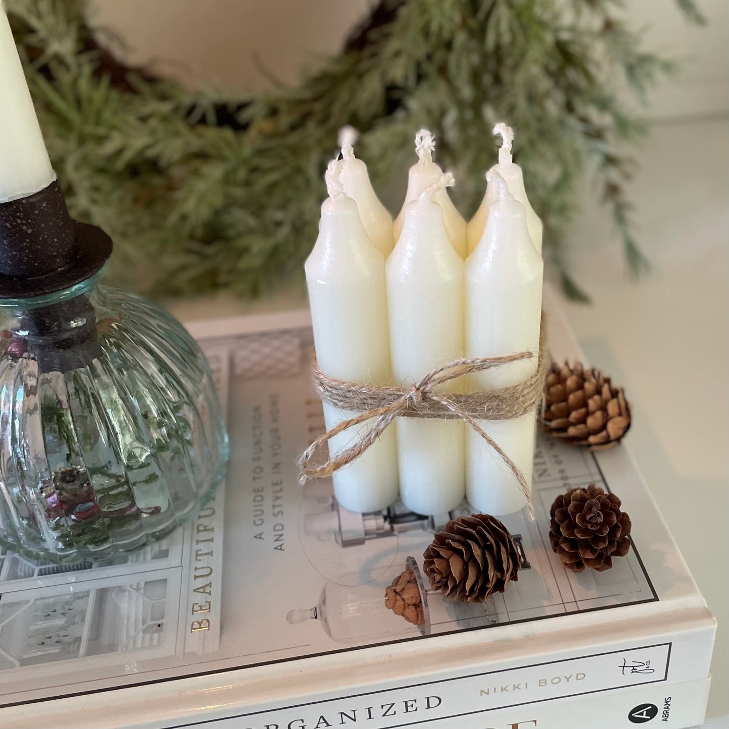 Bundle of six short Danish style dinner candles tied with jute cord, styled on a book with pine cones and candle holder.