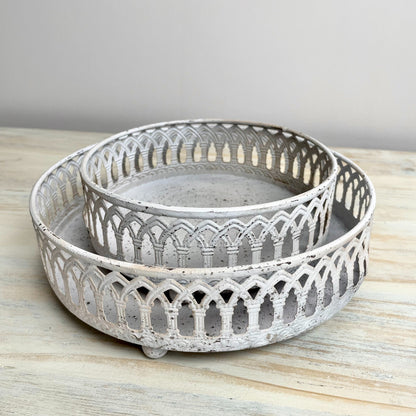 Two decorative metal trays with intricate designs on a wooden surface.