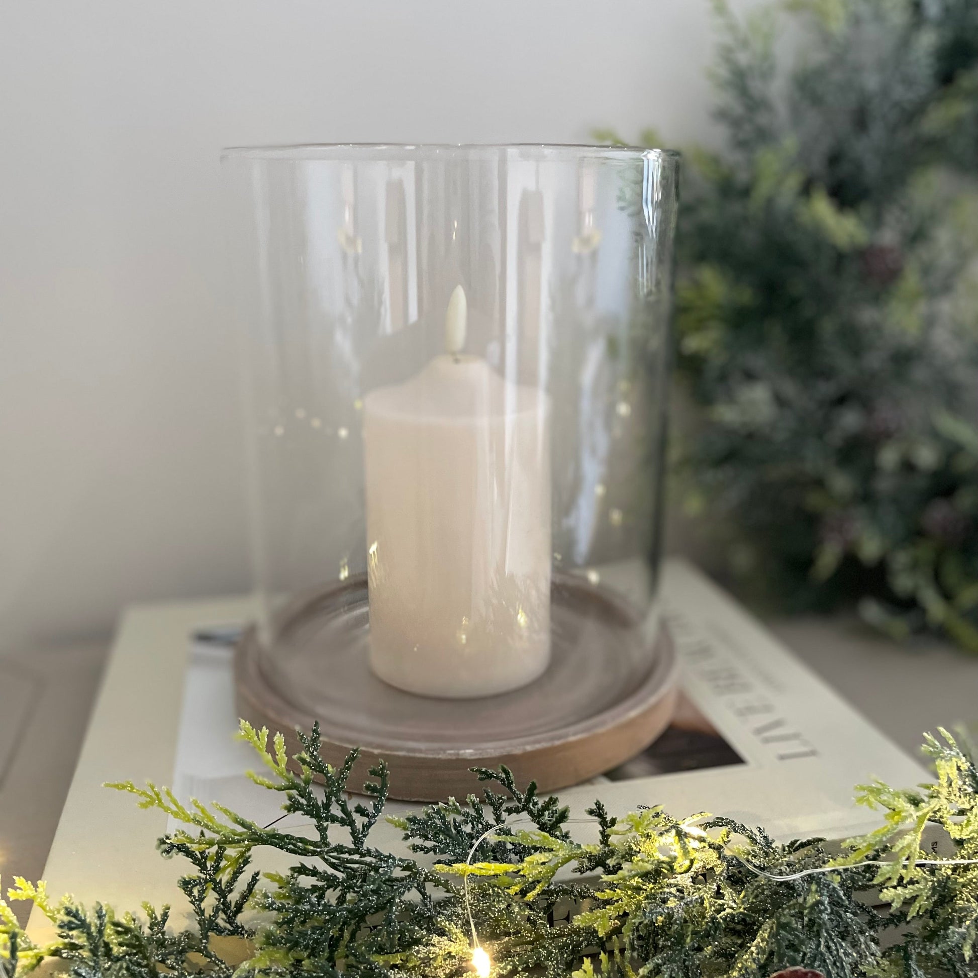 Candle in a stone hurricane lantern styled on a book with greenery on a console table.