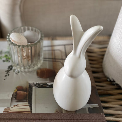 Close up of smooth matte porcelain bunny ornament styled on a book with decorative eggs.