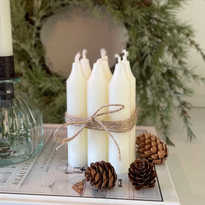 Bundle of six short Danish style dinner candles tied with jute cord, styled on a book with candle holder and wreath.