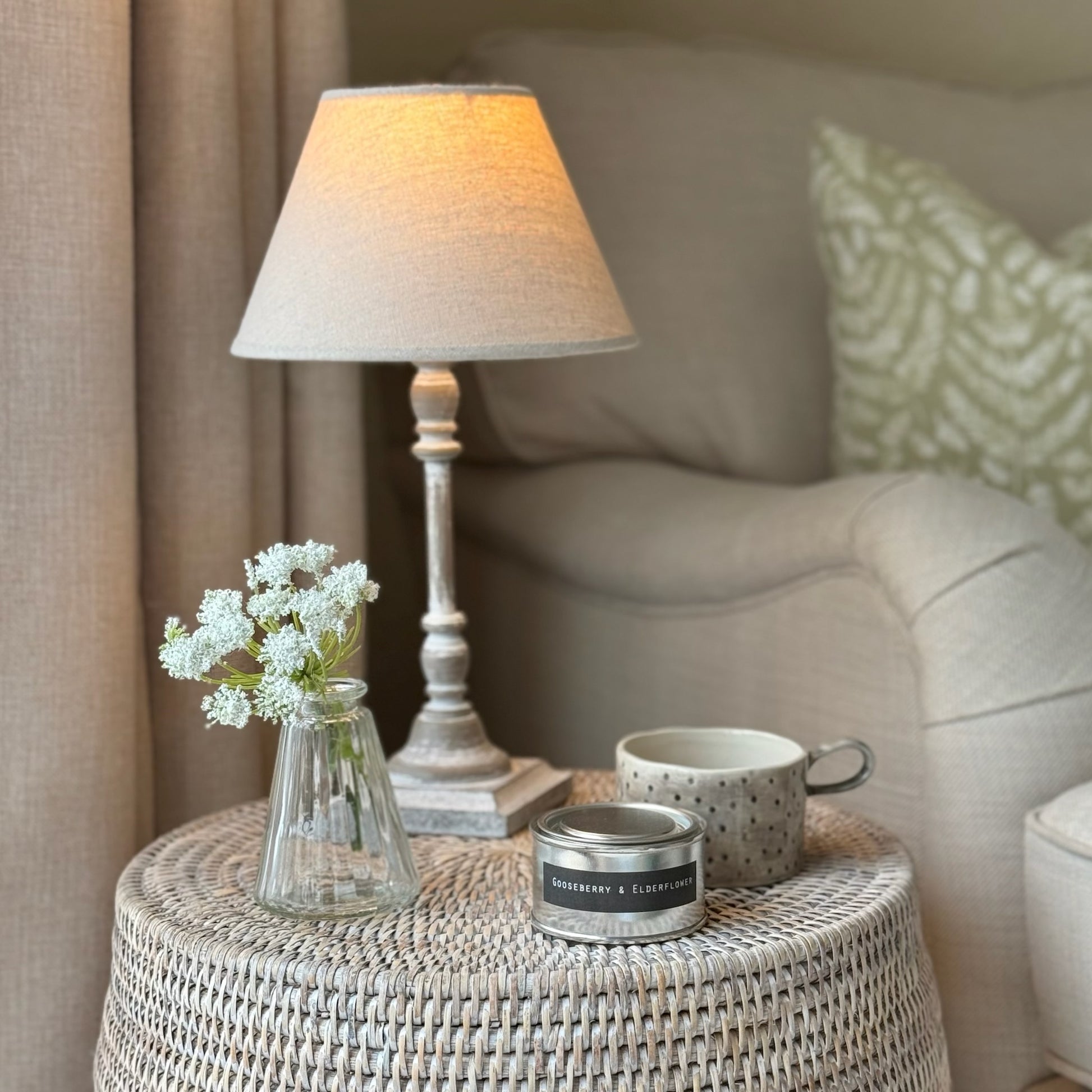 Small table with a lamp, mug, and candle in a cozy living room setting.