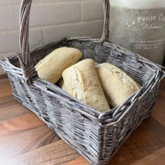 Small wicker basket. Ideal for holding bread or eggs. Rustic woven wicker basket with tall handle and natural finish styled on a kitchen wooden worktop with bread.