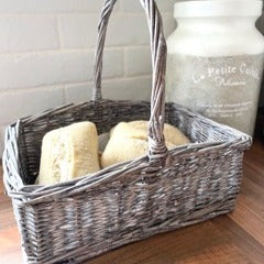 Small wicker basket. Ideal for holding bread or eggs. Rustic woven wicker basket with tall handle and natural finish styled on a kitchen wooden worktop with bread and ceramic pot in the background.