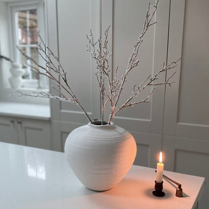 Winter faux branch styled in a white matte ceramic vase on a kitchen worktop.