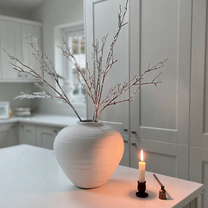 Winter faux branch styled in a white matte ceramic vase next to a candle on a white  kitchen island.