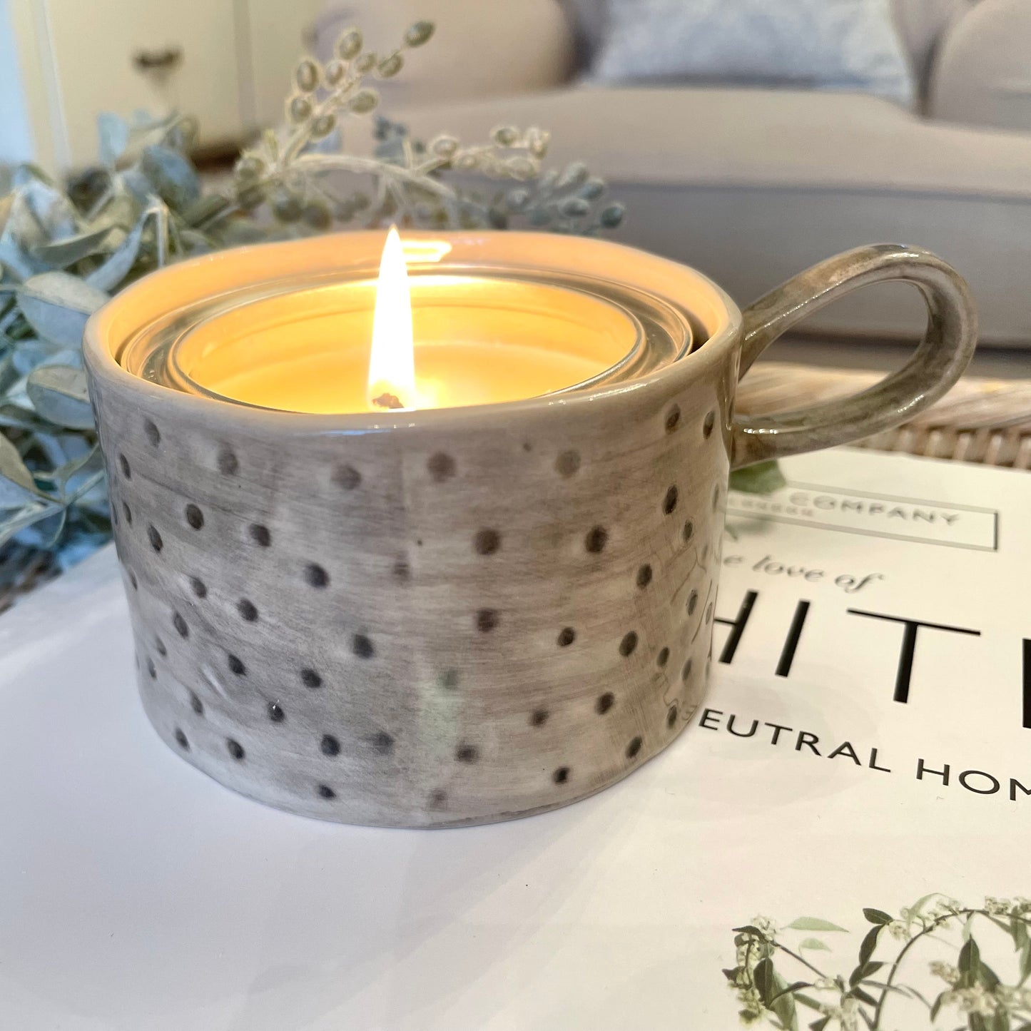 Ceramic spot patterned candle holder with a lit candle on a surface with decorative elements.