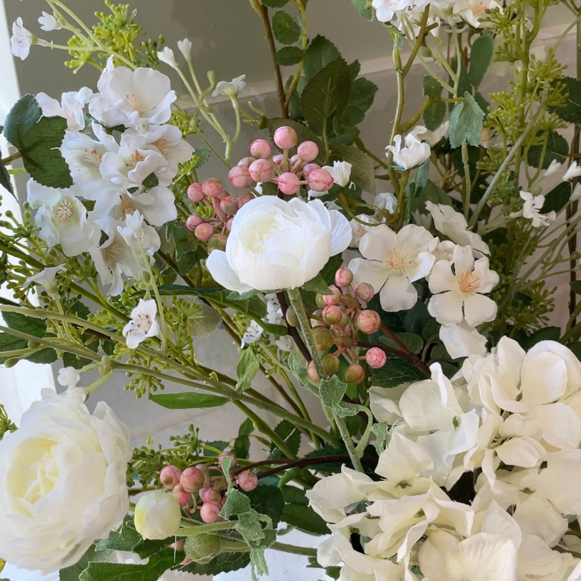 Close up of faux spring bouquet with white ranunculus, wild roses, pink berries, mirabella sprays and a white hydrangea. 