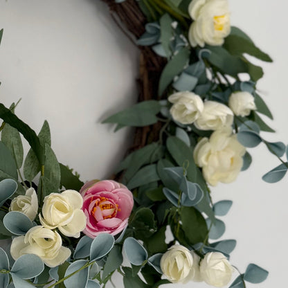 Close up of soft cream and pink roses and foliage on spring grapevine wreath. Styled on a white panelled wall.