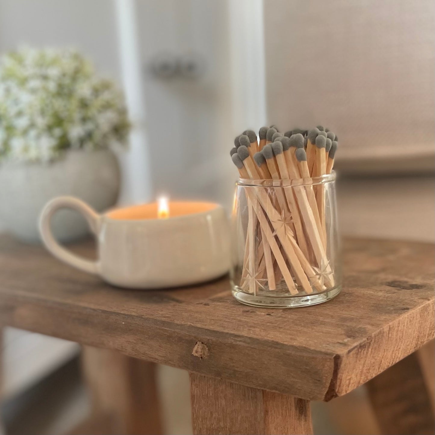Glass match pot with etched star detail, grey matches, and hidden striker pad on the base. Styled next to candle holder and hebe pot on a wooden stool.