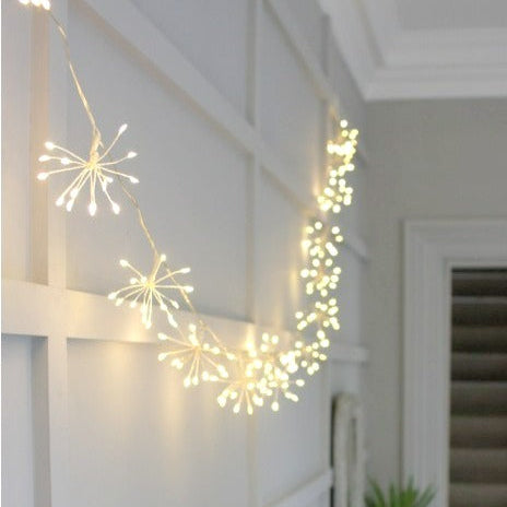 Warm white starburst string lights draped along a rustic mantelpiece, creating a soft festive glow indoors.