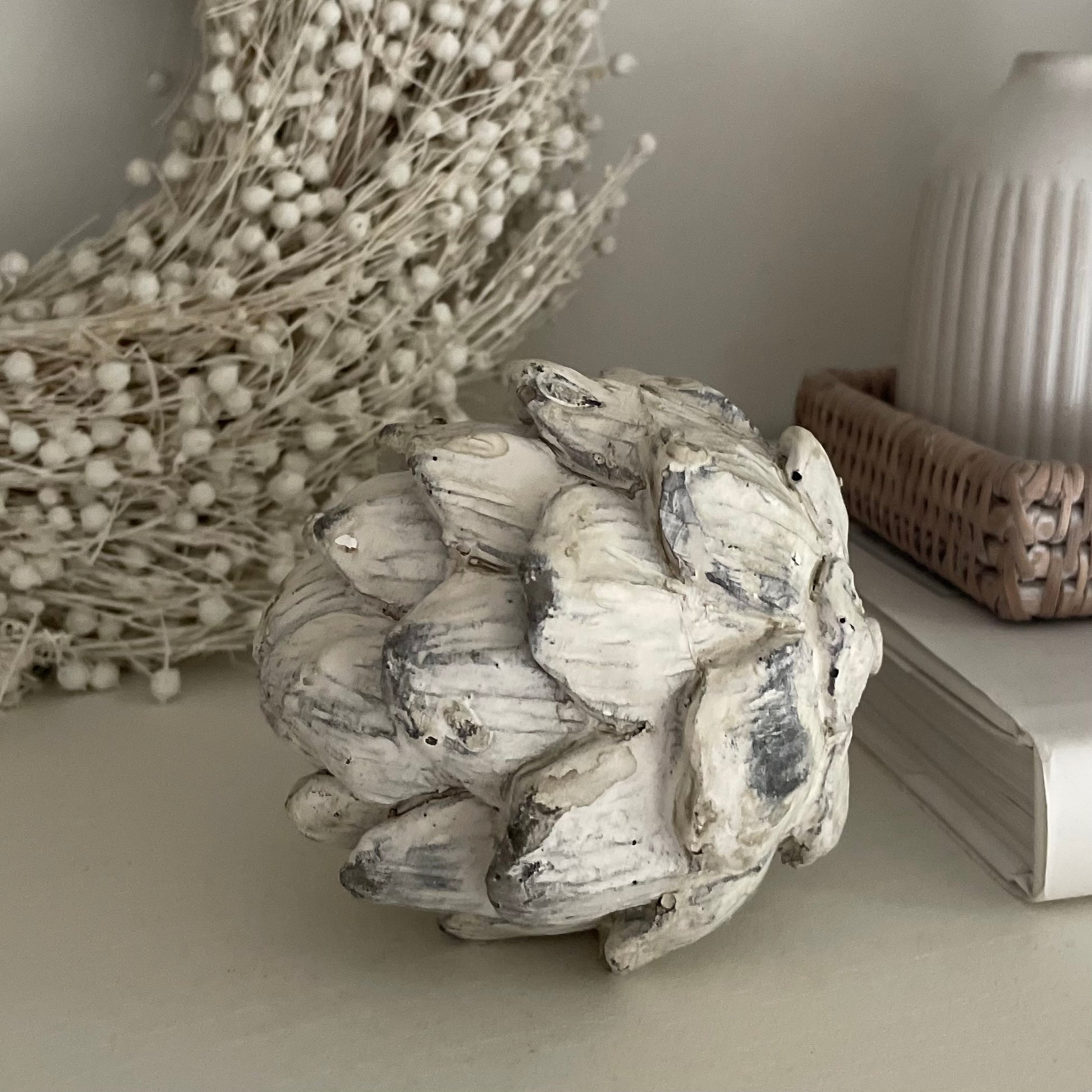 Antique white stone effect decorative artichoke. Styled on a shelf with a white wreath and book.