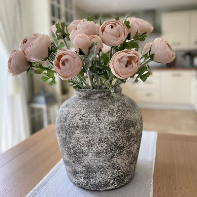 Earthy distressed stone Valentina Vase styled with green foliage on a wooden dining table in a kitchen.