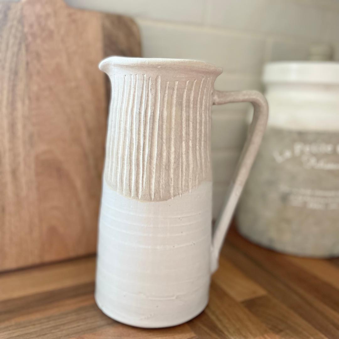 Rustic stoneware jug with light grey textured top and off white gloss glazed base, styled on a wooden work top.