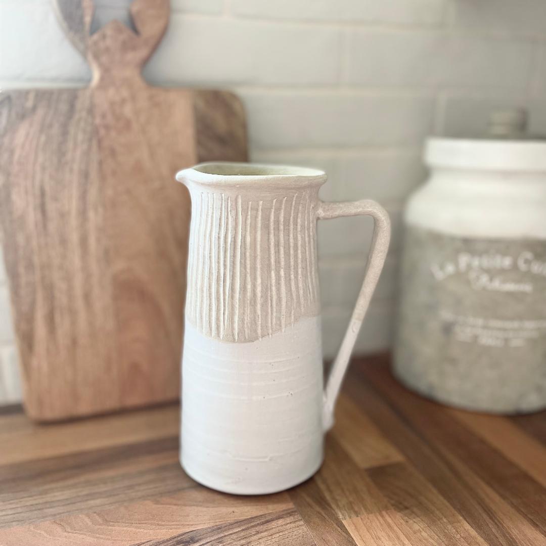 Rustic stoneware jug with light grey textured top and off white gloss glazed base, styled by a wooden chopping on a kitchen worktop.