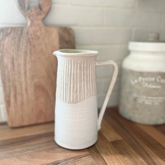 Rustic stoneware jug with light grey textured top and off white gloss glazed base, styled by a wooden chopping on a kitchen worktop.