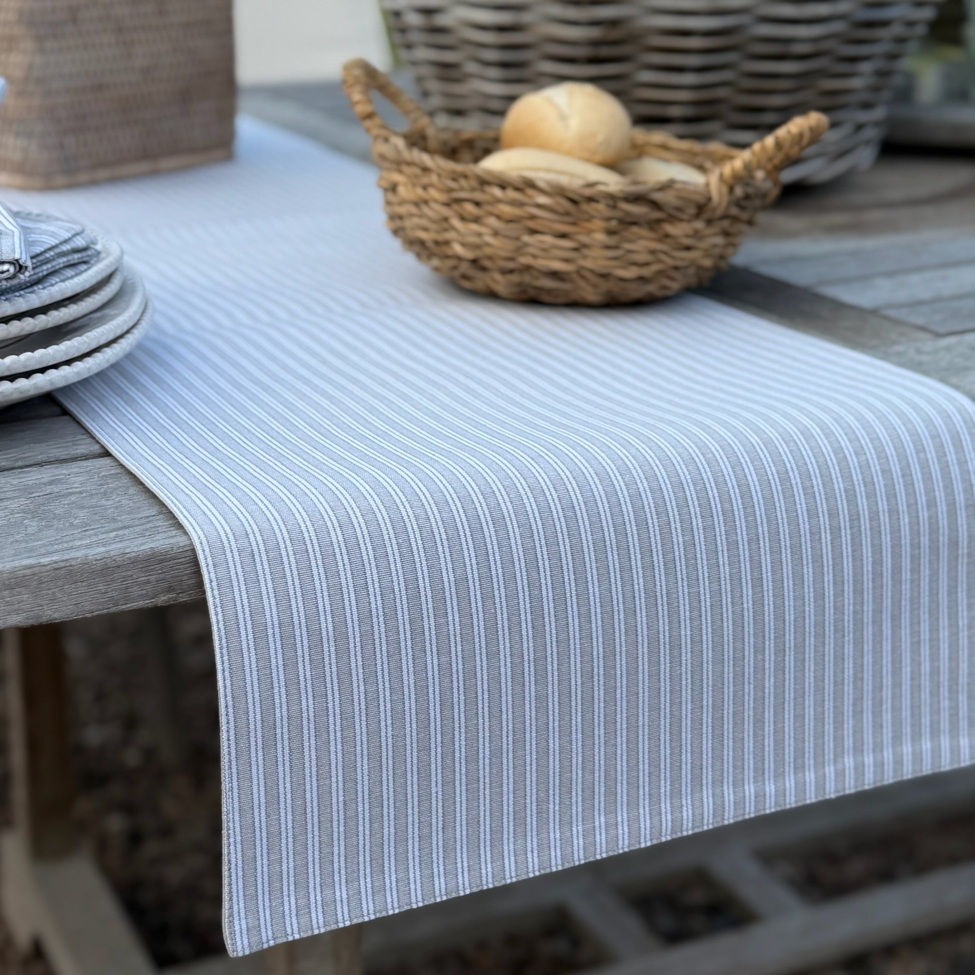 Striped table runner on a wooden table with a woven basket containing bread.