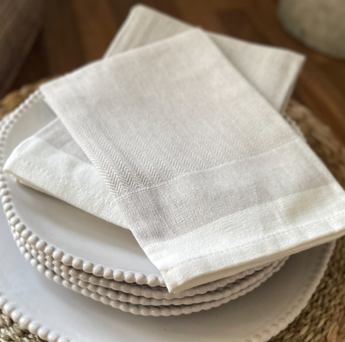 Taupe cotton napkins with woven herringbone pattern. Styled on beaded white plates.
