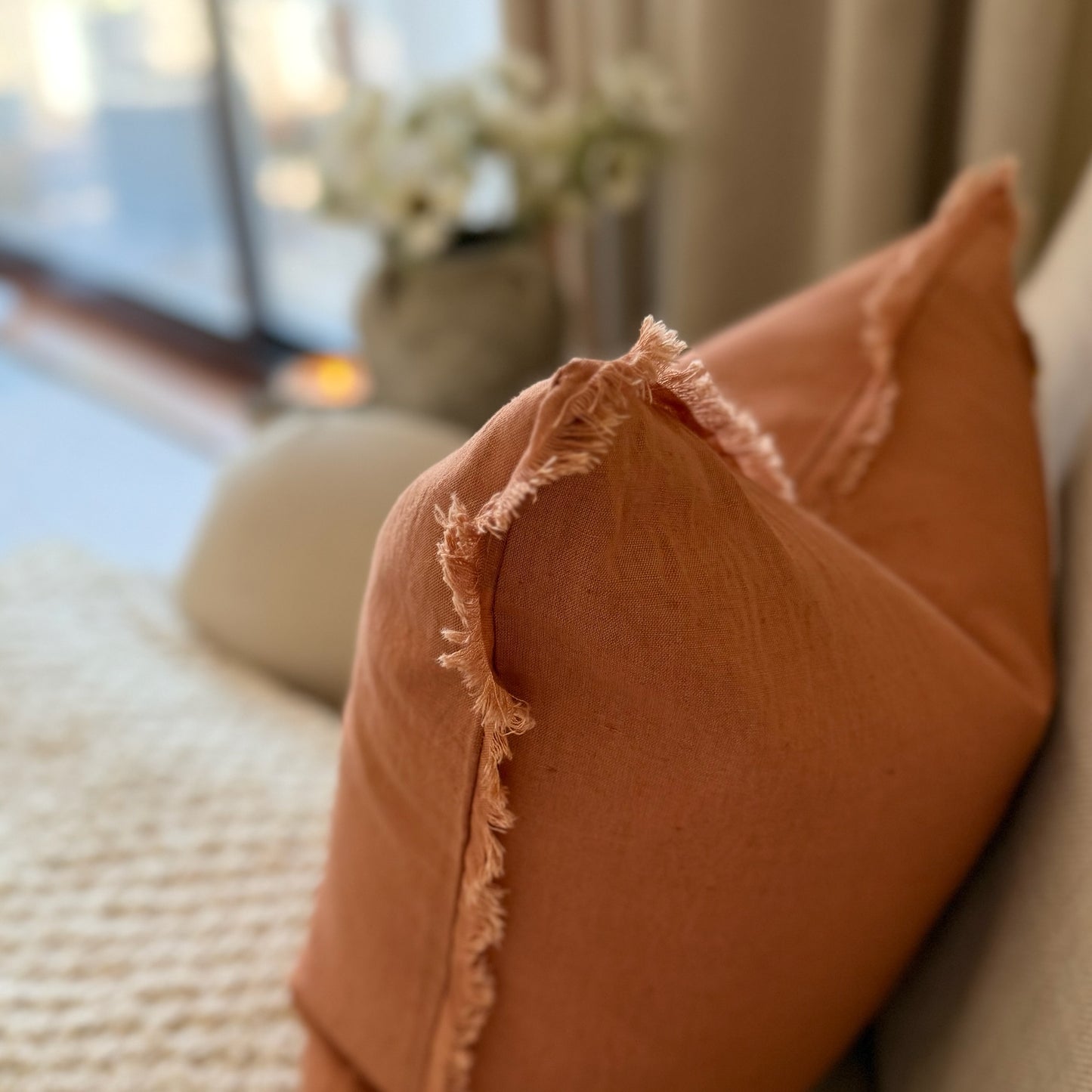 Close-up of a terracotta coloured cushion with frayed edges on a blurred indoor background.