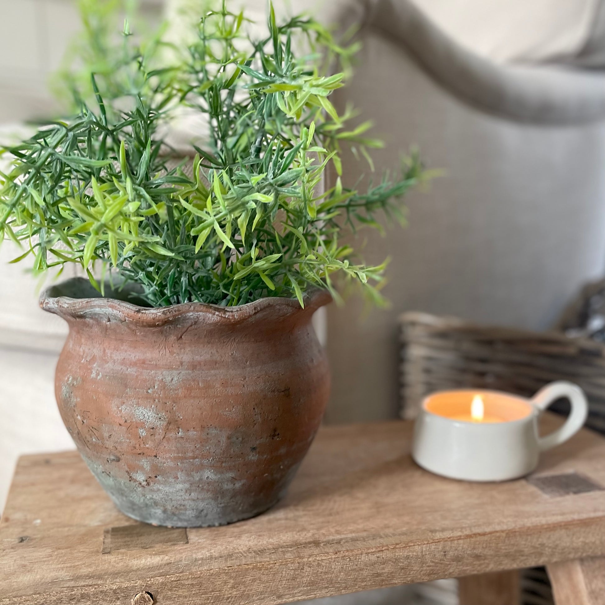 Pie crust edge terracotta pot styled, with a faux plant and candle on a wooden decorative stool.