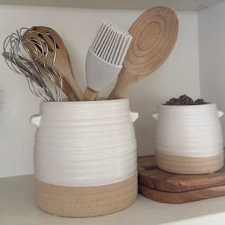 Two tone pot holding kitchen utensils on kitchen shelf.
