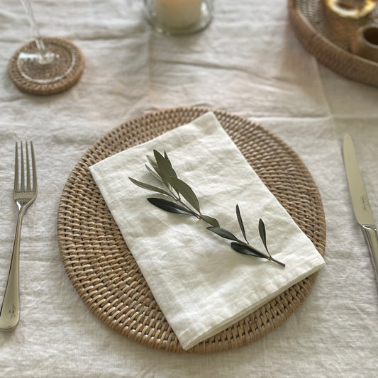 100% natural white linen napkin styled with tableware on a matching white linen tablecloth on a dining table.