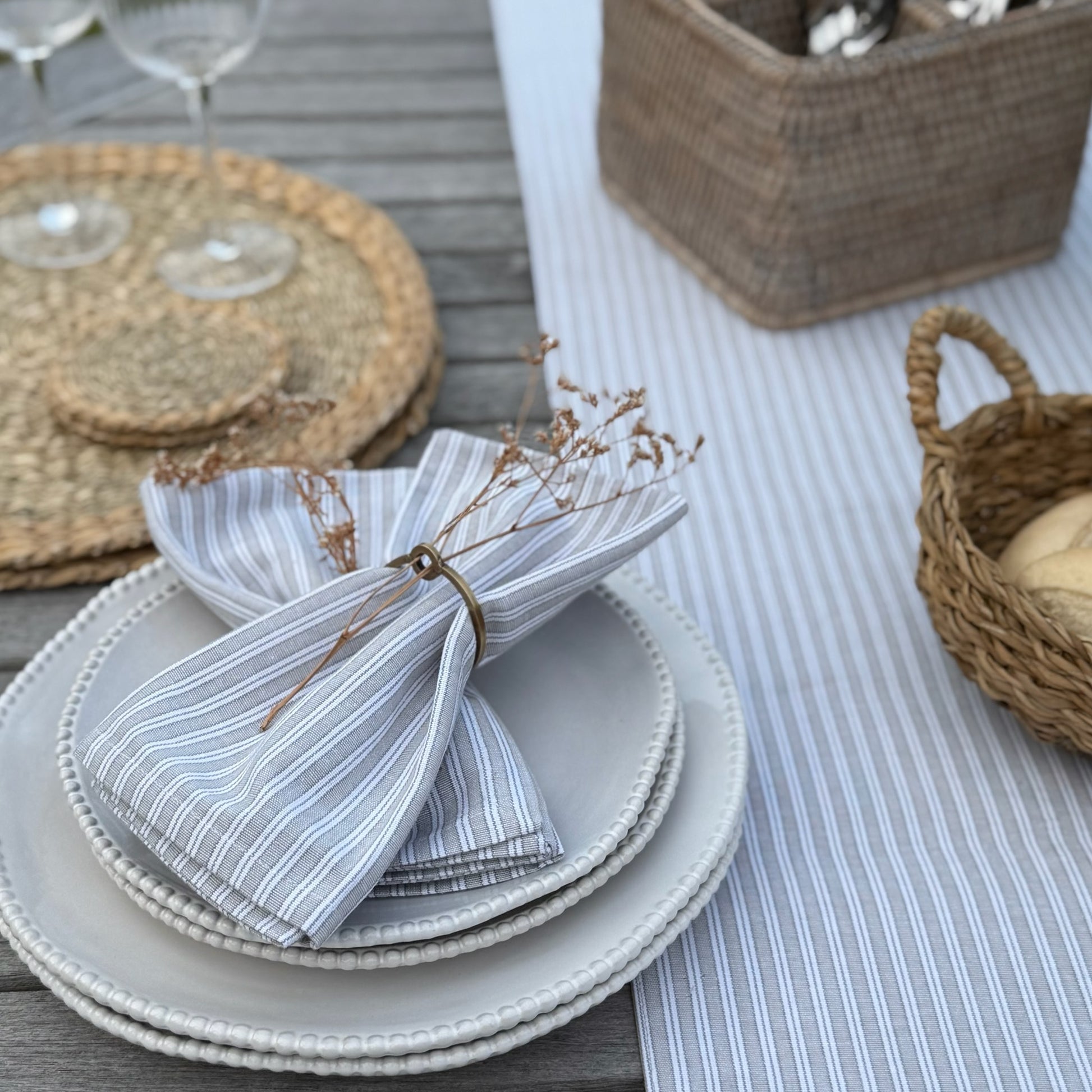 Set of stacked plates with a striped napkin on a table with woven placemats and baskets.